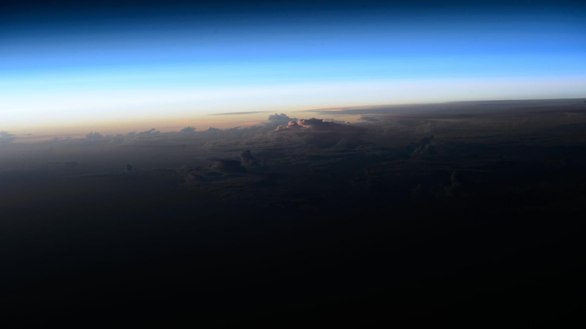 Sunrise breaking above a layer of clouds, photographed from orbit.